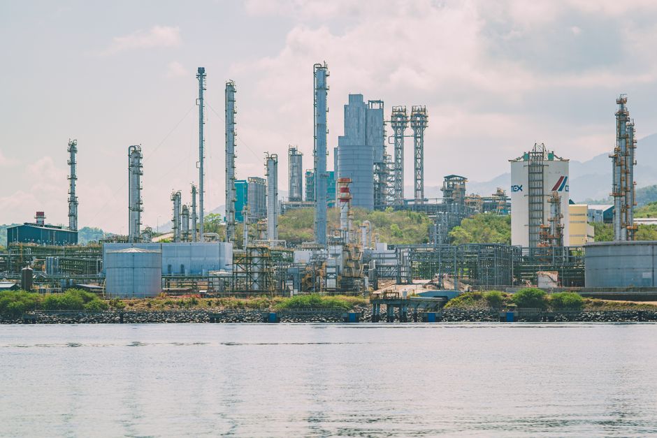 A large industrial refinery complex with tall chimneys by the waterfront under a clear sky