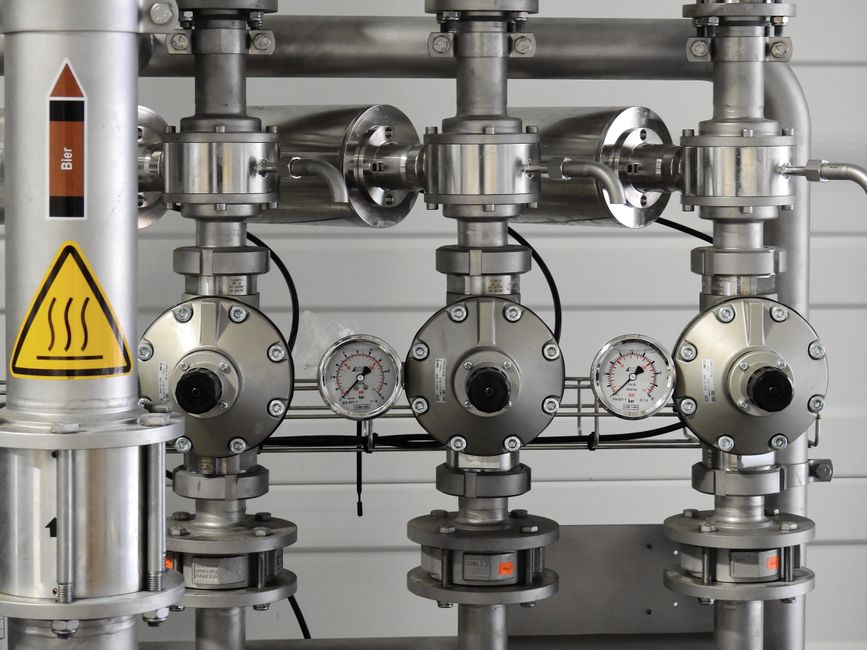 Industrial steel pipelines with pressure gauges in an energy facility, representing the critical oil infrastructure at risk from Middle East chokepoint disruptions.