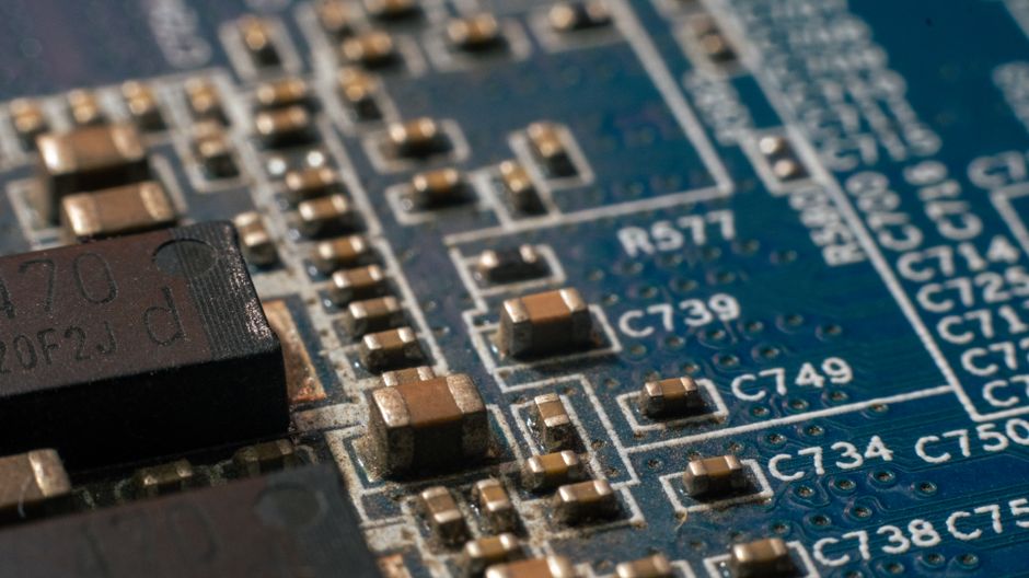 Macro close-up of a circuit board with electronic components and copper traces, representing semiconductor manufacturing.