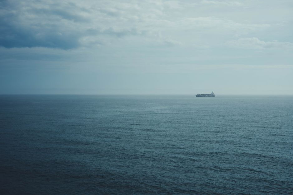 A cargo ship navigating the open ocean under a cloudy sky, illustrating maritime shipping routes threatened by Middle East conflict.