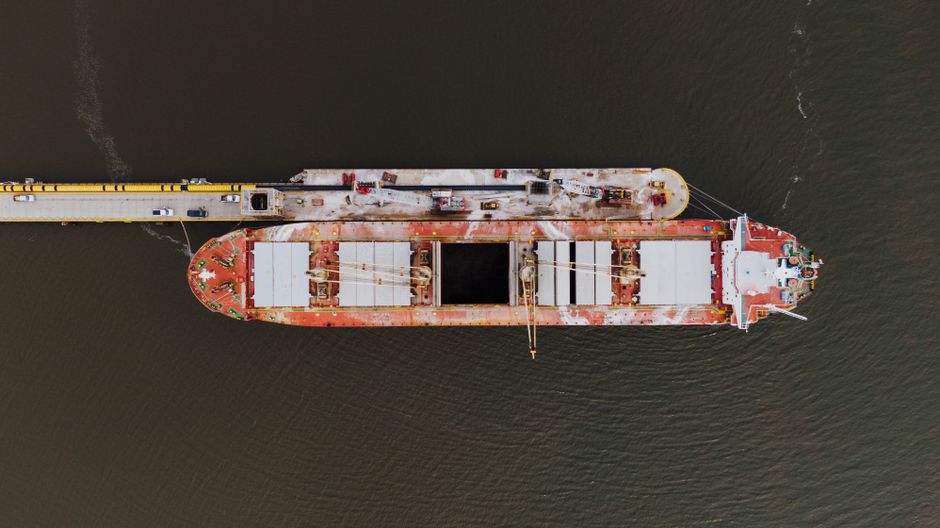 Drone view of a barge moored on rippled ocean near a dock, illustrating maritime shipping in constrained waters.