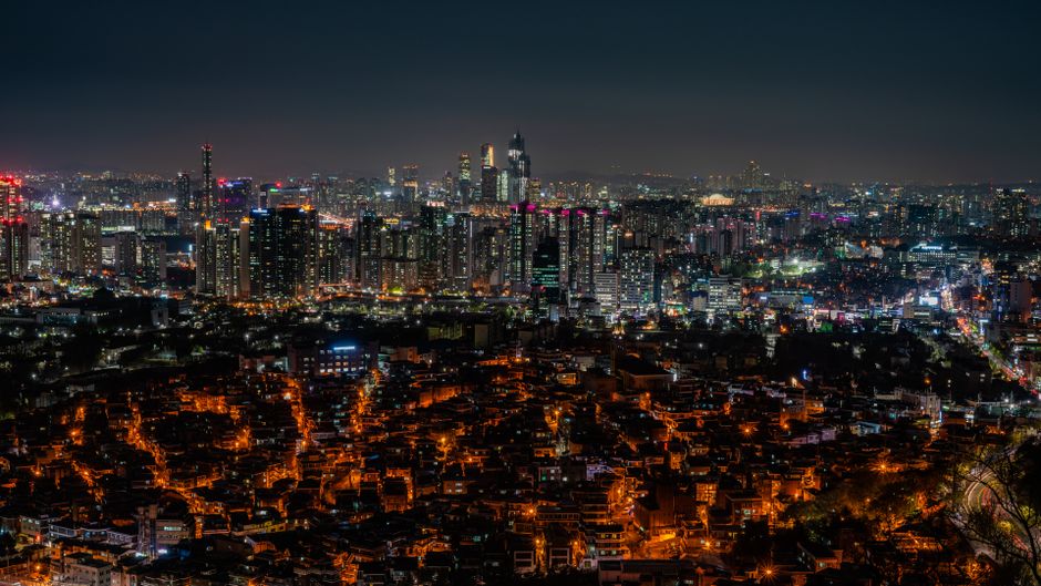 Nighttime city skyline of illuminated skyscrapers and buildings, representing a modern Asian financial and technology hub.