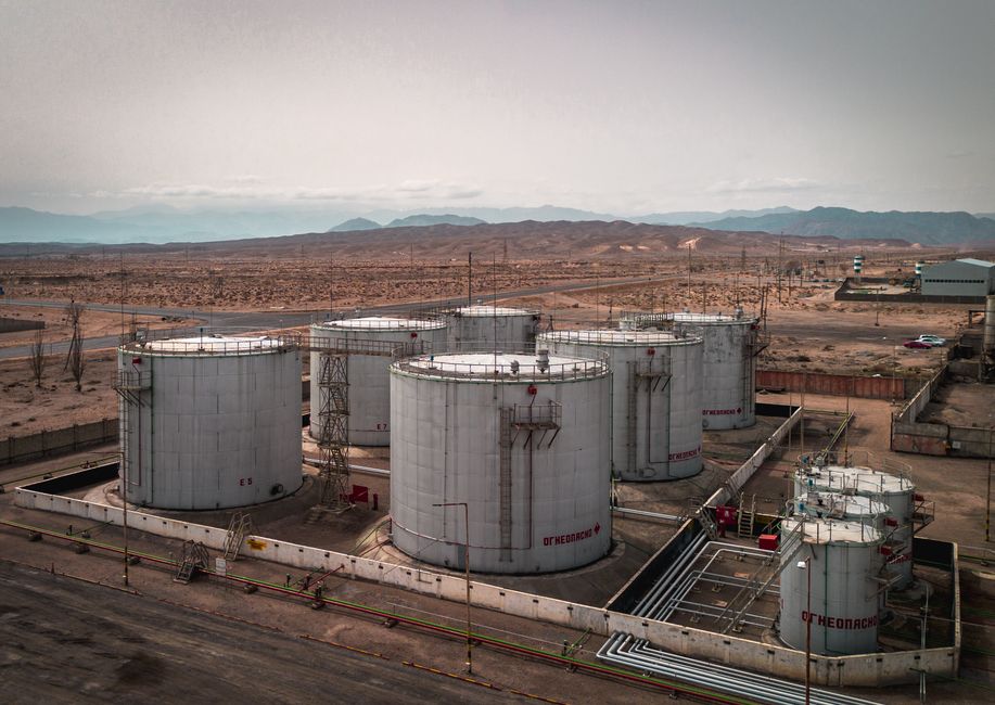 Aerial view of large industrial oil tanks in a desert landscape with mountains in the distance.