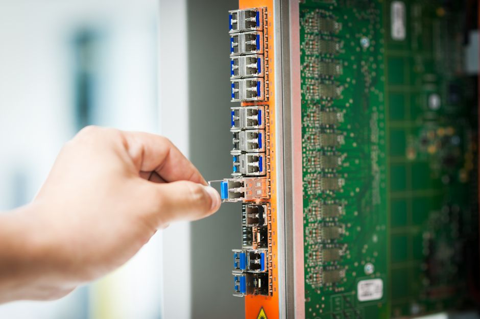 Engineer connecting a cable into a network server port in a data center, representing AI infrastructure investment