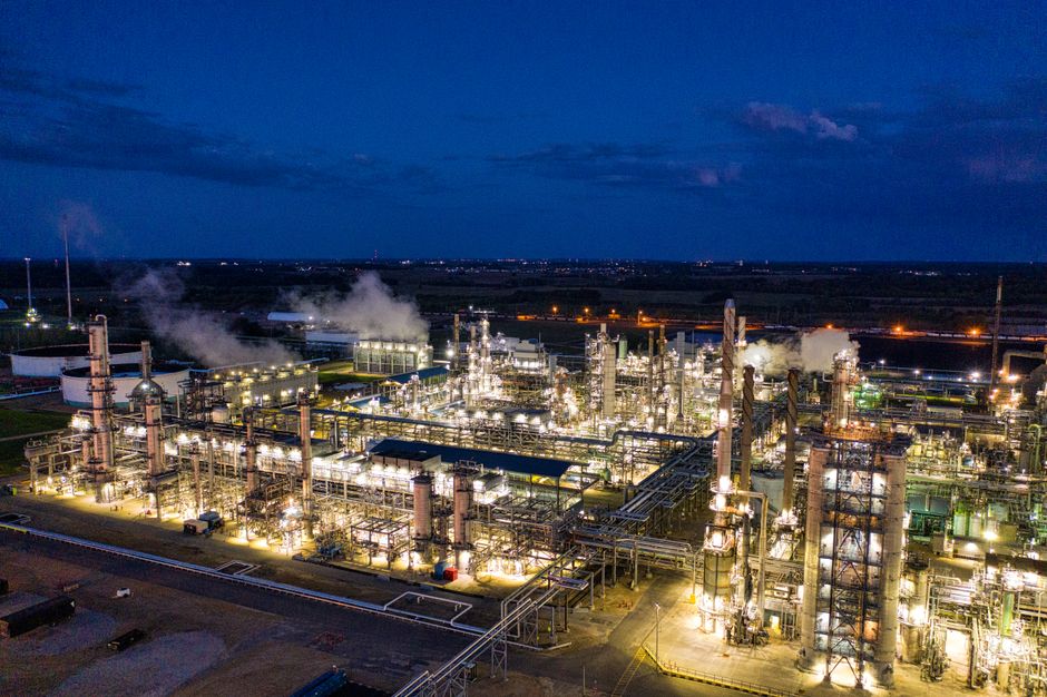 Aerial night view of a large oil refinery with illuminated smokestacks and storage tanks, illustrating the energy infrastructure affected by Middle East supply disruptions.
