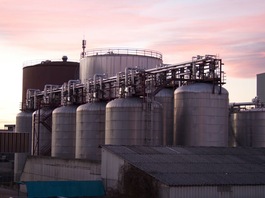 Industrial oil refinery with large stainless steel storage tanks and piping at dusk.