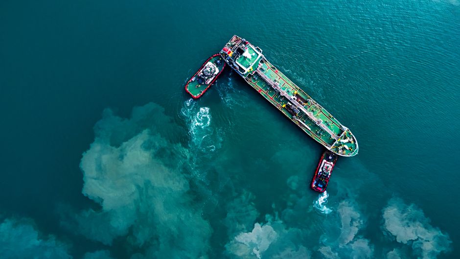 A cargo ship and tugboats move through a maritime trade corridor as shipping and energy risks rise.