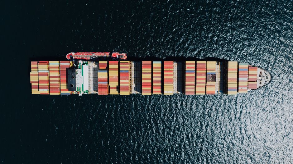 Aerial view of a fully loaded cargo ship on the open sea, illustrating the vulnerability of global maritime trade chokepoints like the Strait of Hormuz.