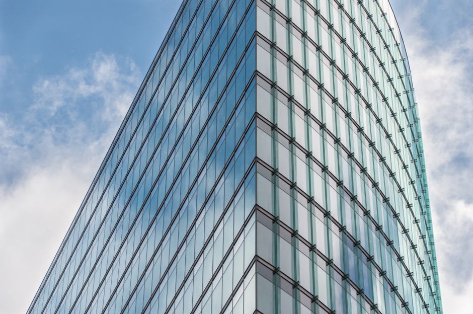 A sleek glass skyscraper reflecting blue sky and clouds, representing modern financial infrastructure.