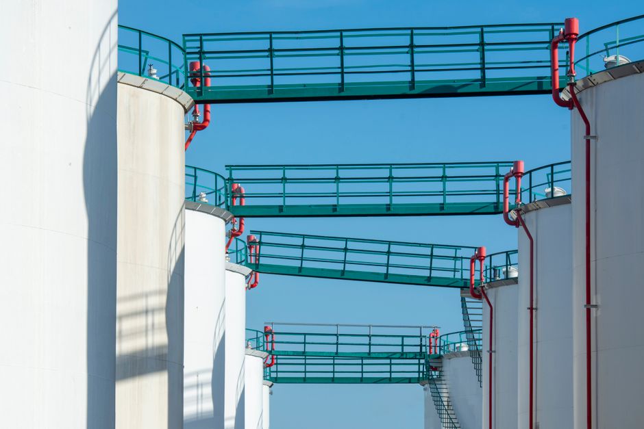 Industrial storage tanks against a blue sky, representing the energy infrastructure exposed to the Hormuz supply shock.