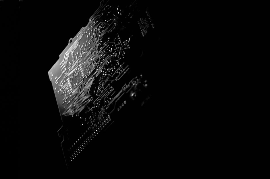 Monochrome close-up of a PCB circuit board highlighting intricate electronic pathways and components.