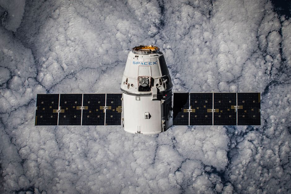A SpaceX Dragon spacecraft in orbit above Earth with a cloud backdrop, representing space technology and orbital operations.