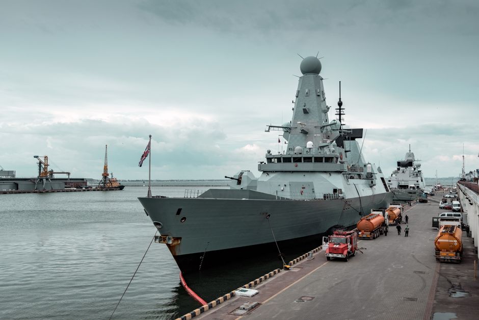 A navy destroyer docked at a harbor under a cloudy sky