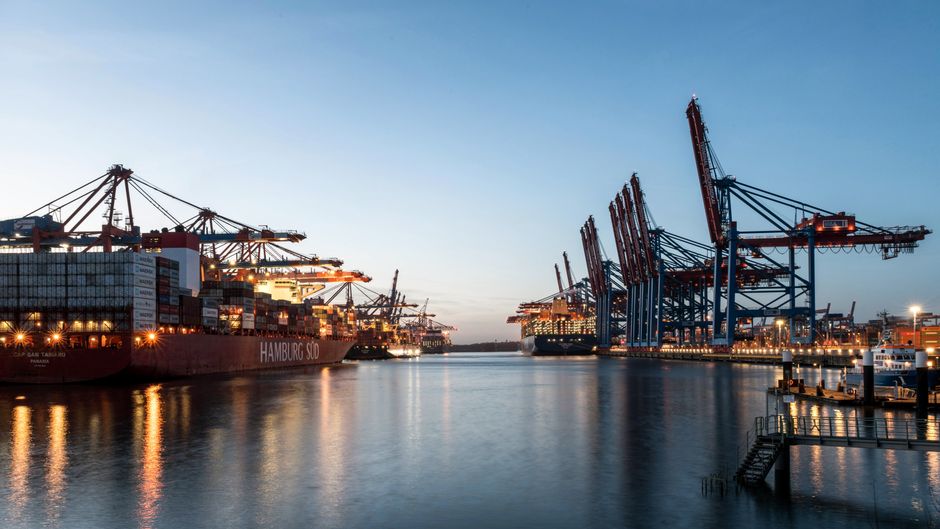 Cargo ships and cranes at a busy port terminal at dusk, illustrating global maritime trade throughput.