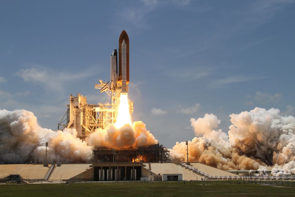 A NASA space shuttle launches with fiery liftoff, ascending into the sky amid plumes of smoke, representing SpaceX's record $75 billion IPO and the aerospace sector's public-market debut.