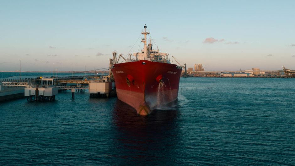 A cargo ship at an industrial port as maritime disruption raises energy and freight risks.