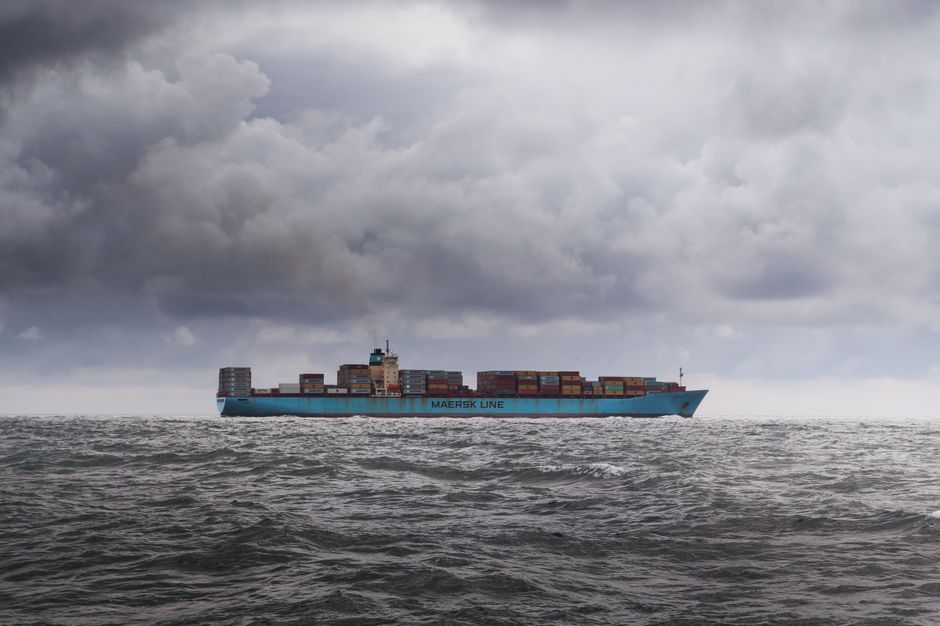 Large cargo ship carrying containers across a cloudy ocean horizon
