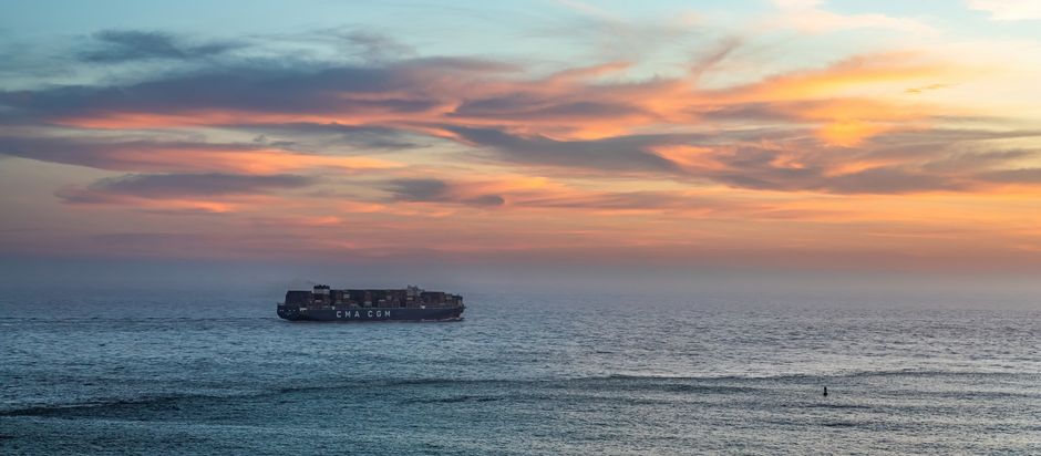 A large cargo ship sailing across open ocean under a warm sunset sky.