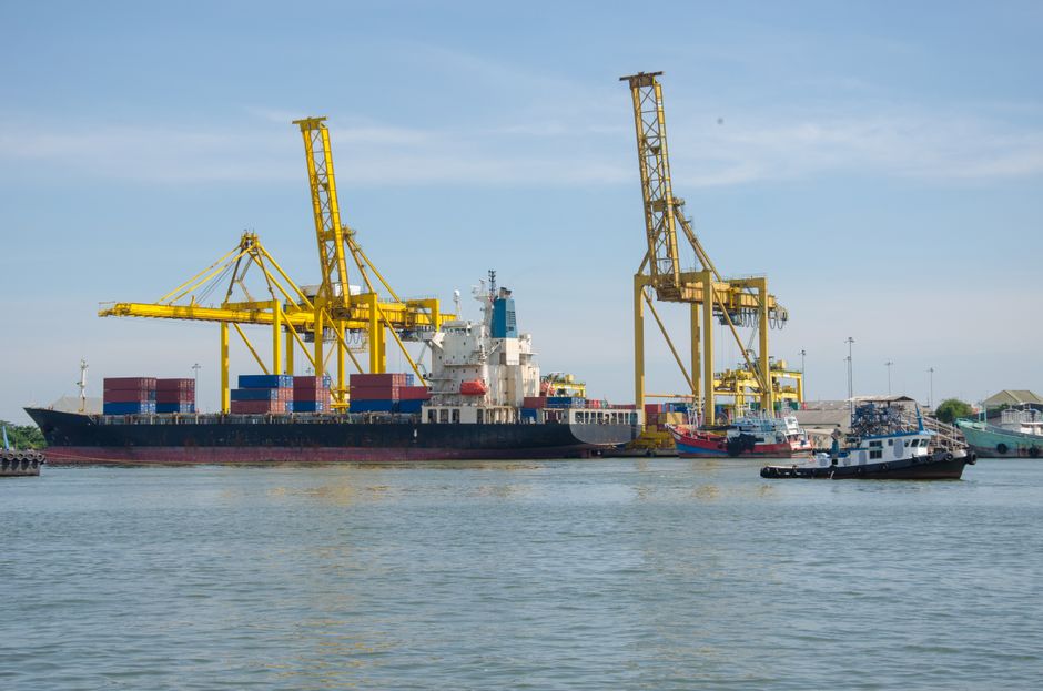 Cargo ship docked at an industrial port with cranes and containers