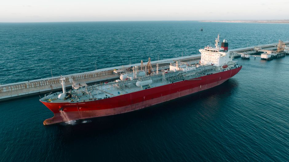 Aerial view of a massive cargo ship docked at a coastal port under clear skies, illustrating maritime shipping through a critical trade corridor.