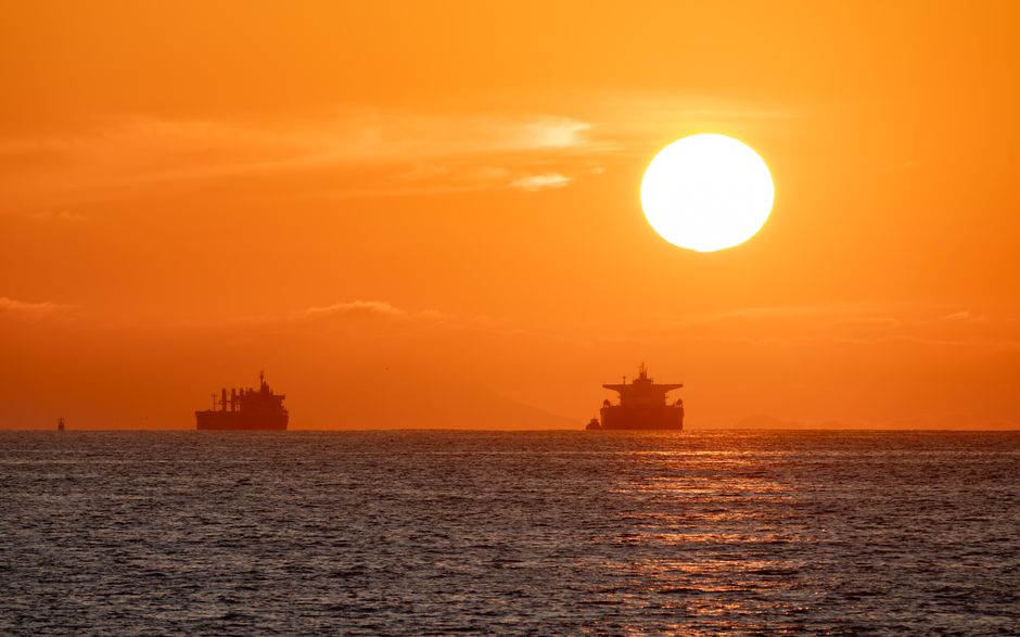 Oil tankers silhouetted against a vibrant sunset over the open sea.
