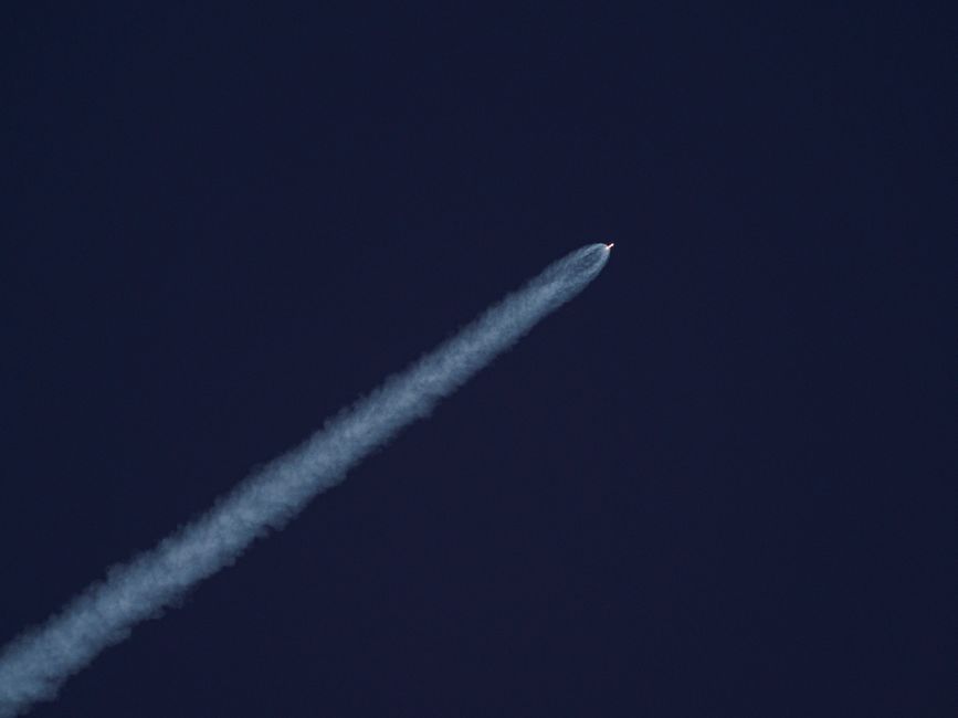 A rocket ascends into the sky leaving a trail of exhaust smoke against a clear blue background.