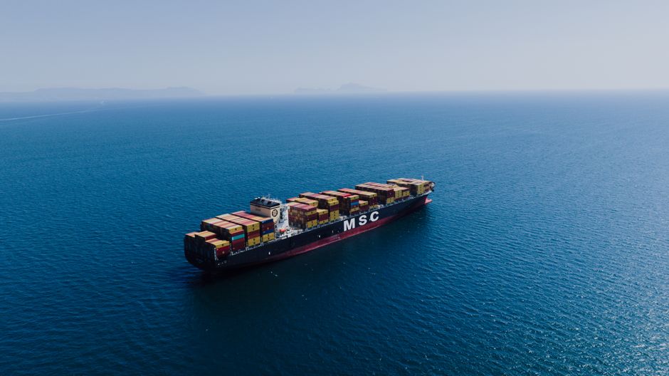 Aerial view of a loaded container ship sailing on open ocean under clear skies