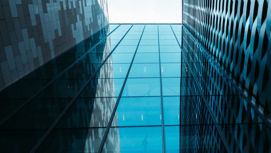 Modern glass and steel skyscraper facade viewed from below against a clear sky, representing corporate technology headquarters.