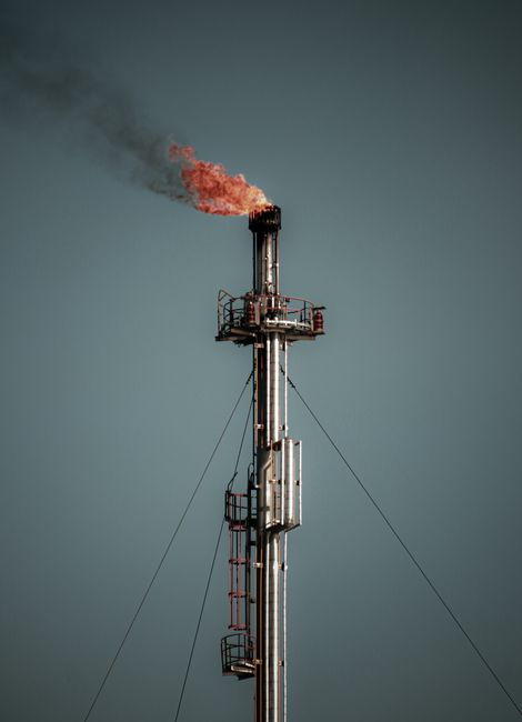 Industrial flare stack releasing flame and smoke against a clear sky