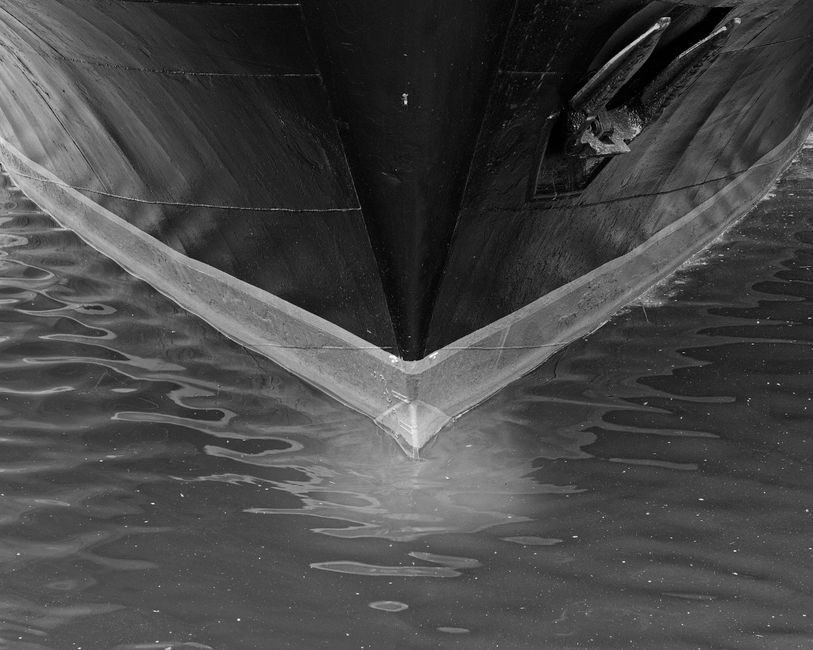 A ship's bow cutting through open water in dramatic black and white, symbolizing the maritime energy supply chain navigating dangerous chokepoints.