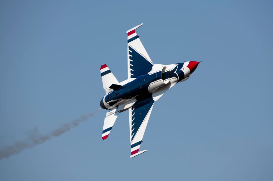A high-speed military jet performing an aerobatic maneuver against a clear sky