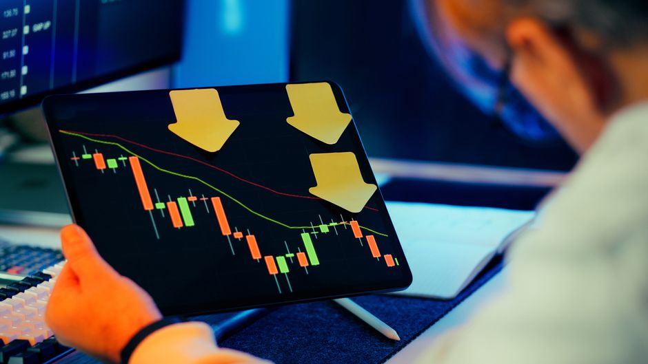A professional analyzing a bearish stock market trend on a tablet, showing downward price charts.