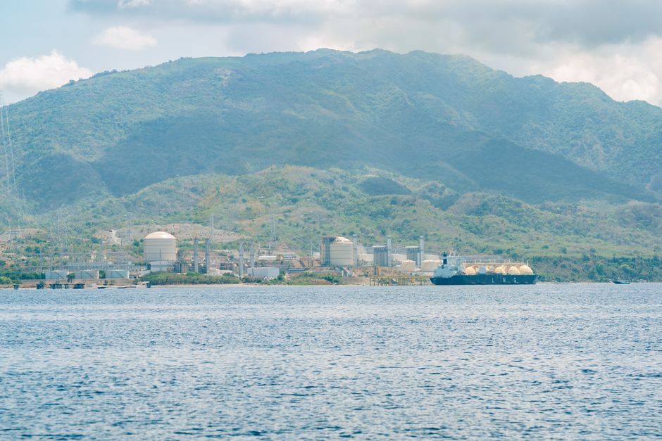 Coastal industrial facility with a tanker ship against a mountainous backdrop