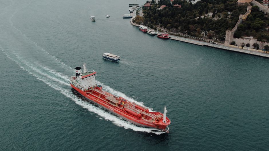 A large cargo ship transiting a narrow strait under cloudy skies, illustrating the chokepoint shipping dynamics central to the Hormuz reopening story.