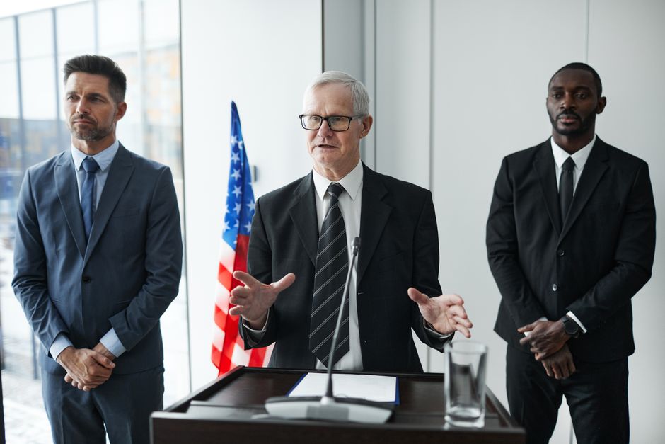 Three professionals speaking at a podium with an American flag backdrop.