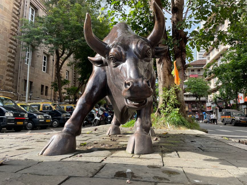 A prominent bull statue amidst a bustling urban street scene.
