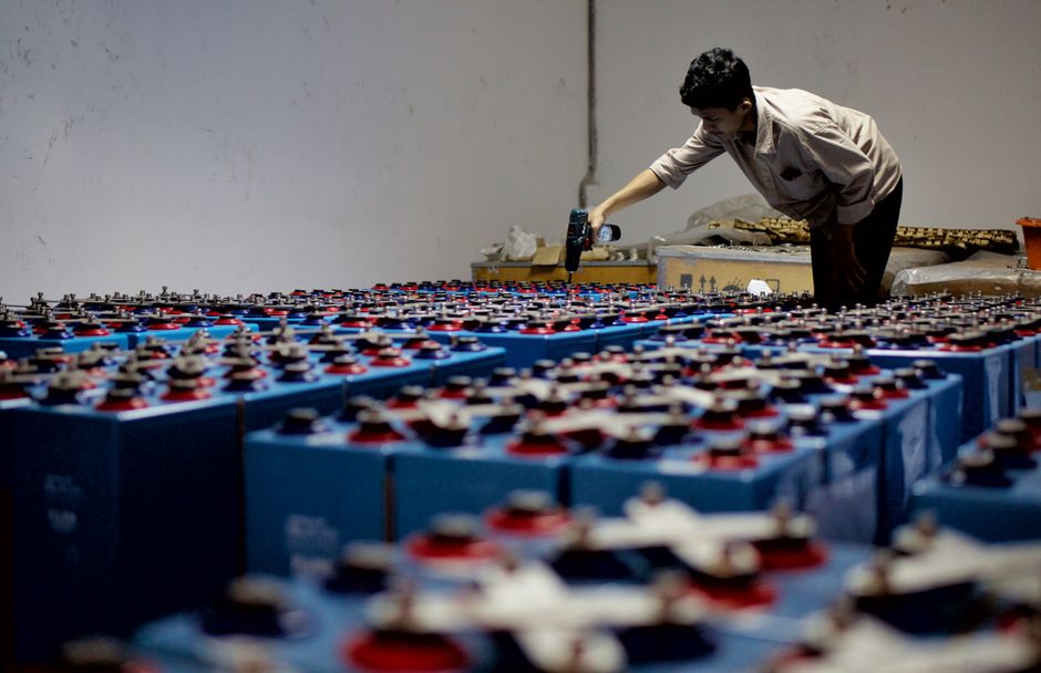 Industrial worker inspecting rows of batteries in a warehouse facility.