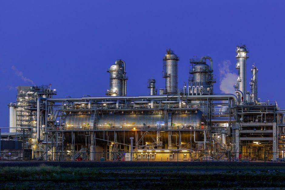 An industrial facility illuminated at dusk, with dramatic lighting against a clear blue sky.