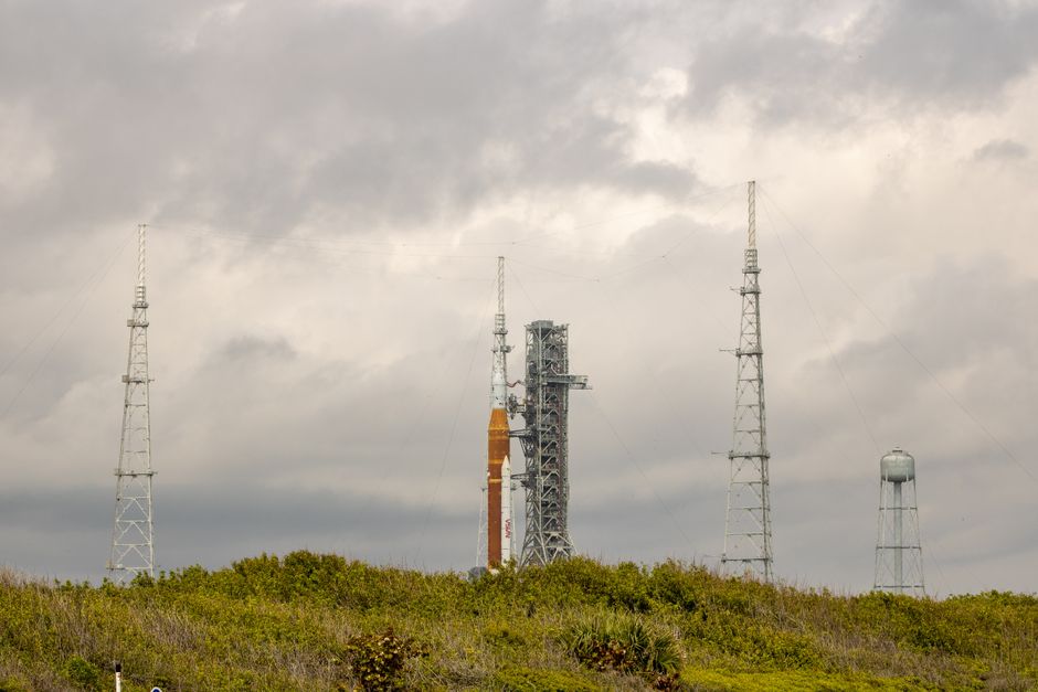 A rocket stands on a launch pad against an overcast sky, surrounded by support structures.