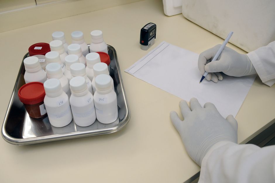 A gloved laboratory technician writes on paper beside medical samples in a research facility.