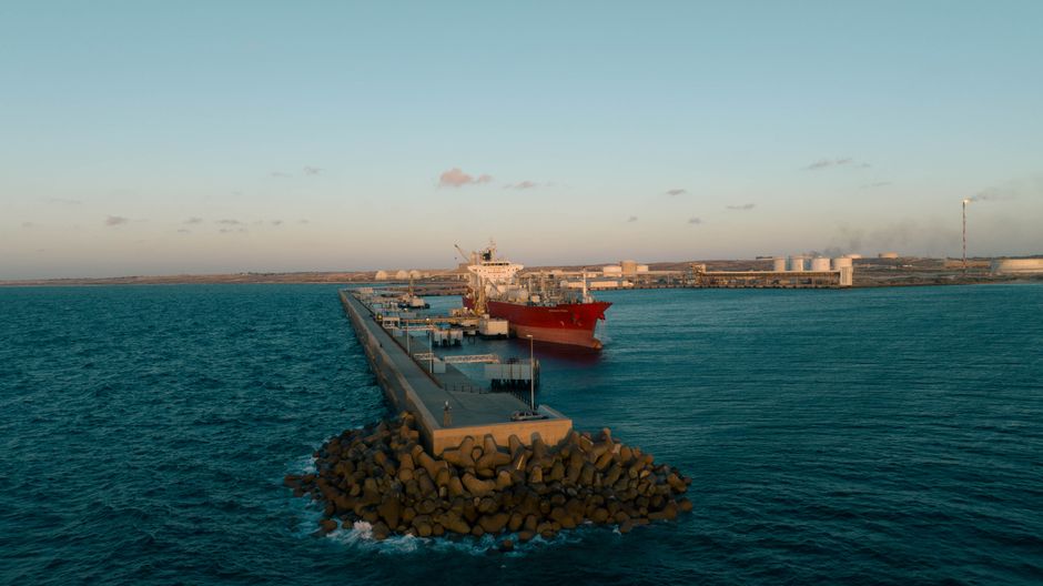 Aerial view of a large cargo ship docked at an industrial harbor, representing the resumption of Gulf crude shipping through the Strait of Hormuz.