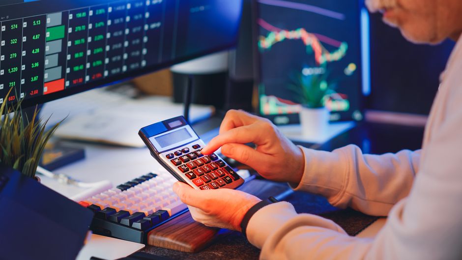 Person using a calculator in a digital office while analyzing market data.