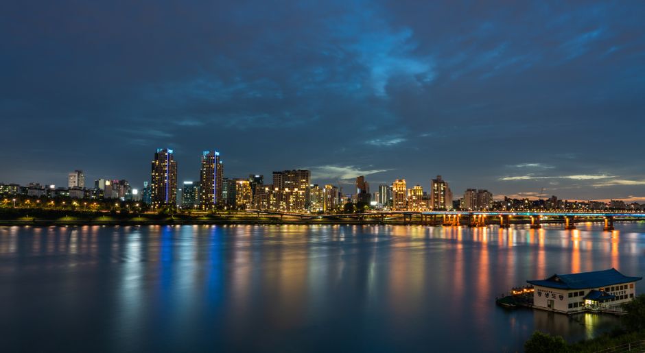 Dramatic twilight view of Seoul skyline with city lights reflecting in the river.