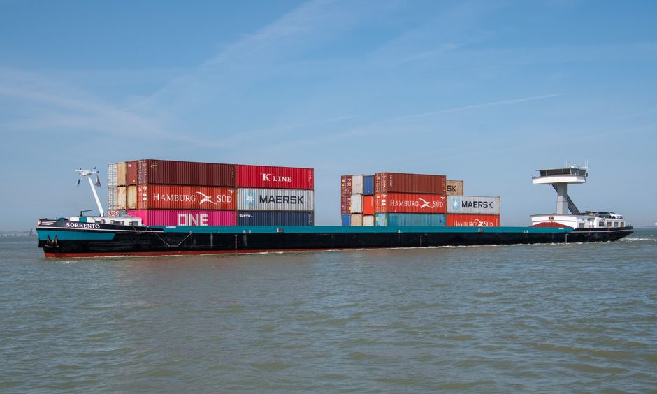 A cargo ship carrying branded containers across the ocean on a clear day, illustrating the maritime trade routes transiting the Strait of Hormuz.