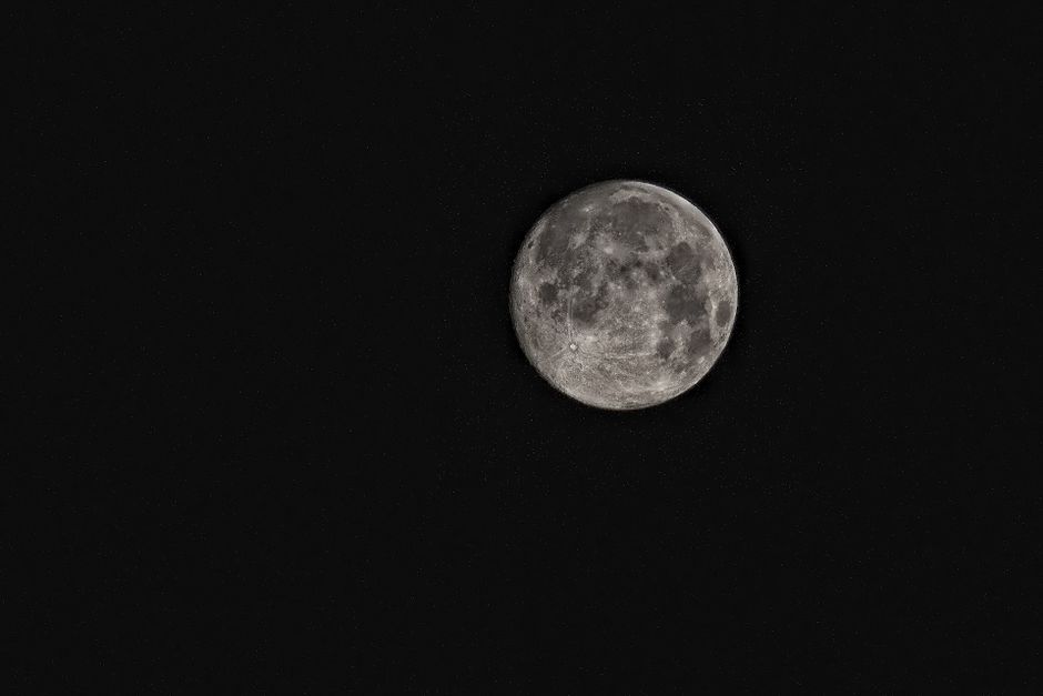 A detailed photograph of the full moon amidst a star-filled night sky.
