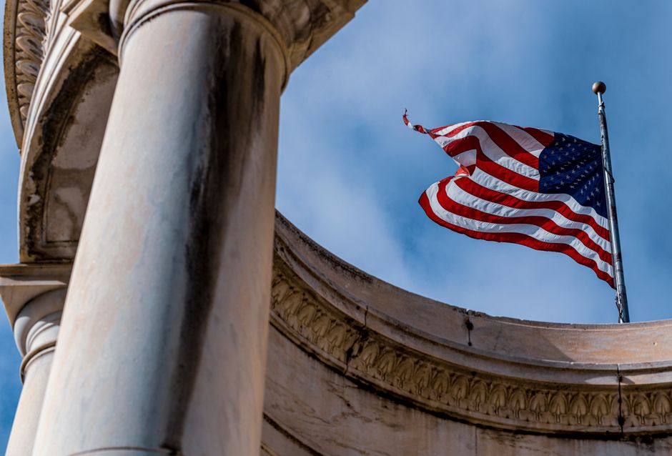American flag waving beside a marble column against a clear blue sky