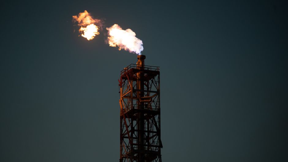 Industrial chimney with a dramatic flame against a dark sky, evoking energy production and geopolitical tension.