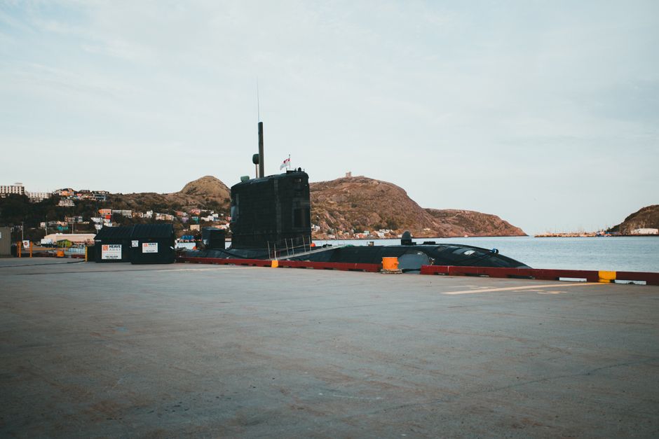 A submarine docked at a pier, surrounded by hills and calm waters.