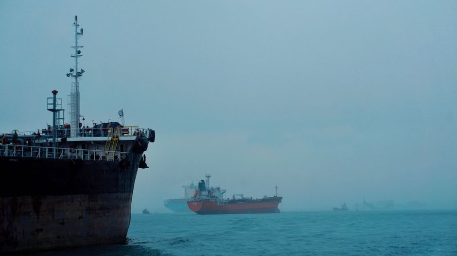 Oil and cargo tankers navigate a foggy ocean shipping lane, illustrating global energy supply chain vulnerability.