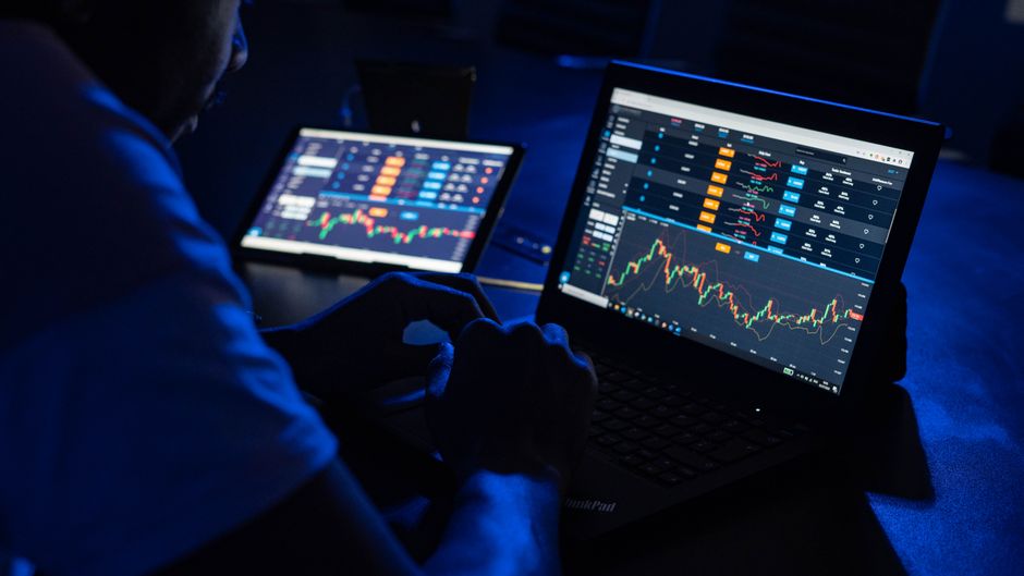 Market participant analyzing financial charts and market depth on multiple laptop screens